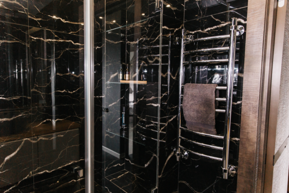 Стены во всей ванной, в том числе ив душевой, а также пол выложены крупной плиткой черного цвета с имитацией трещин мрамора. 