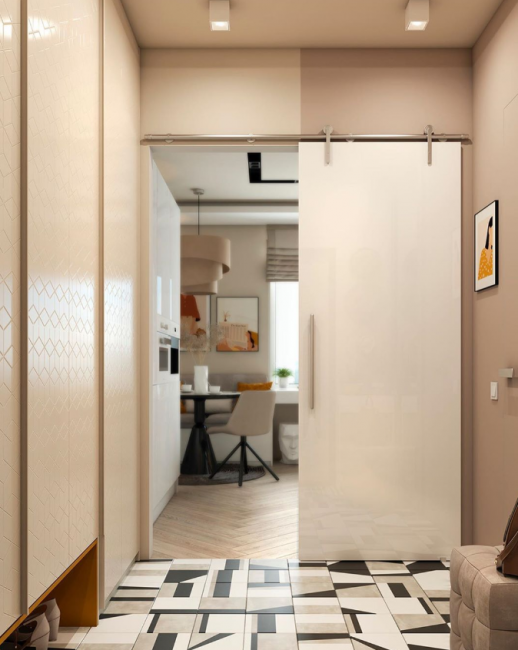 Из коридора в кухню ведет раздвижная дверь. На полу — плитка с оригинальным геометрическим рисунком. 